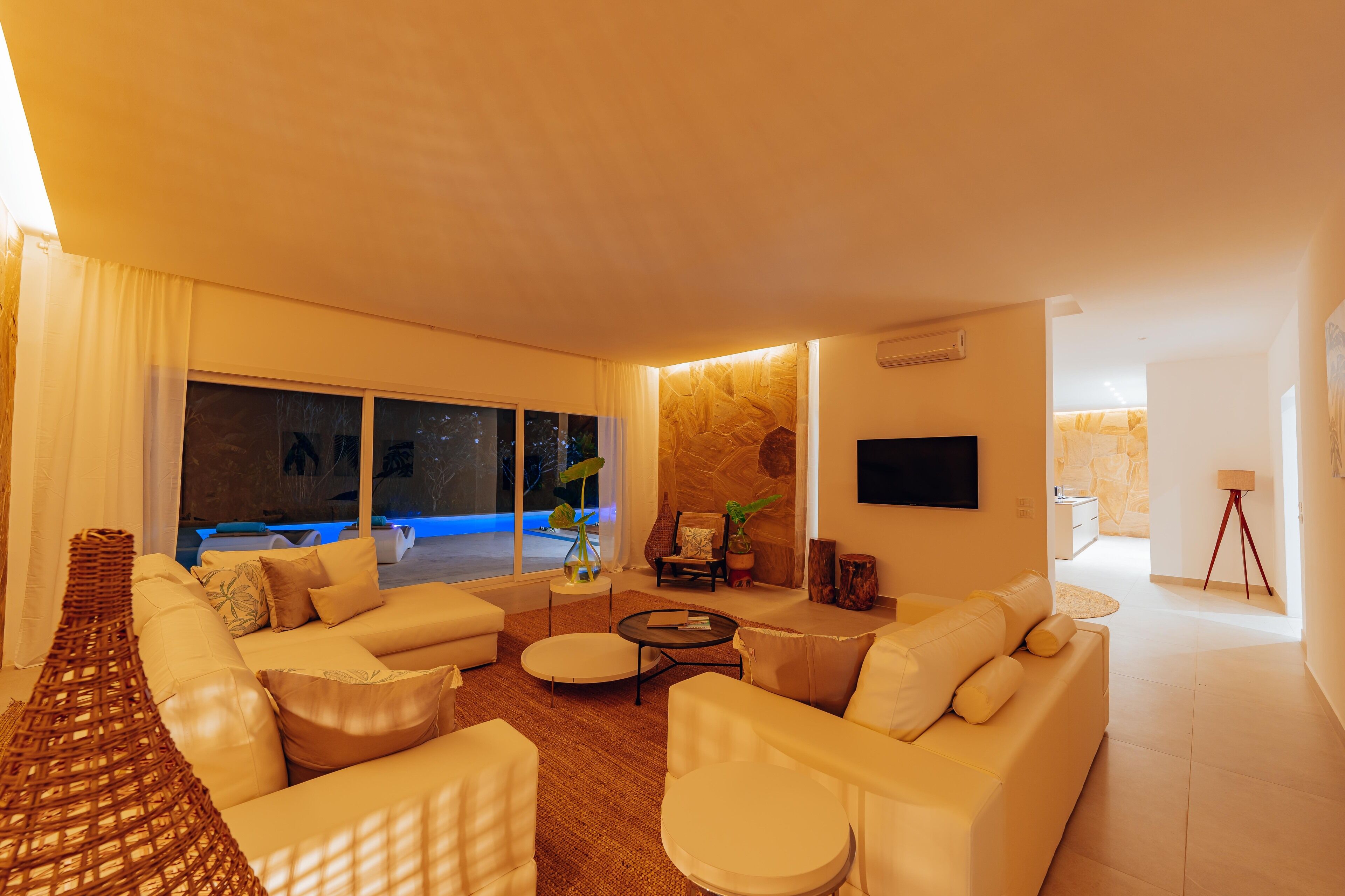 A modern living room with a large sofa, a coffee table, and a view of a pool at night.