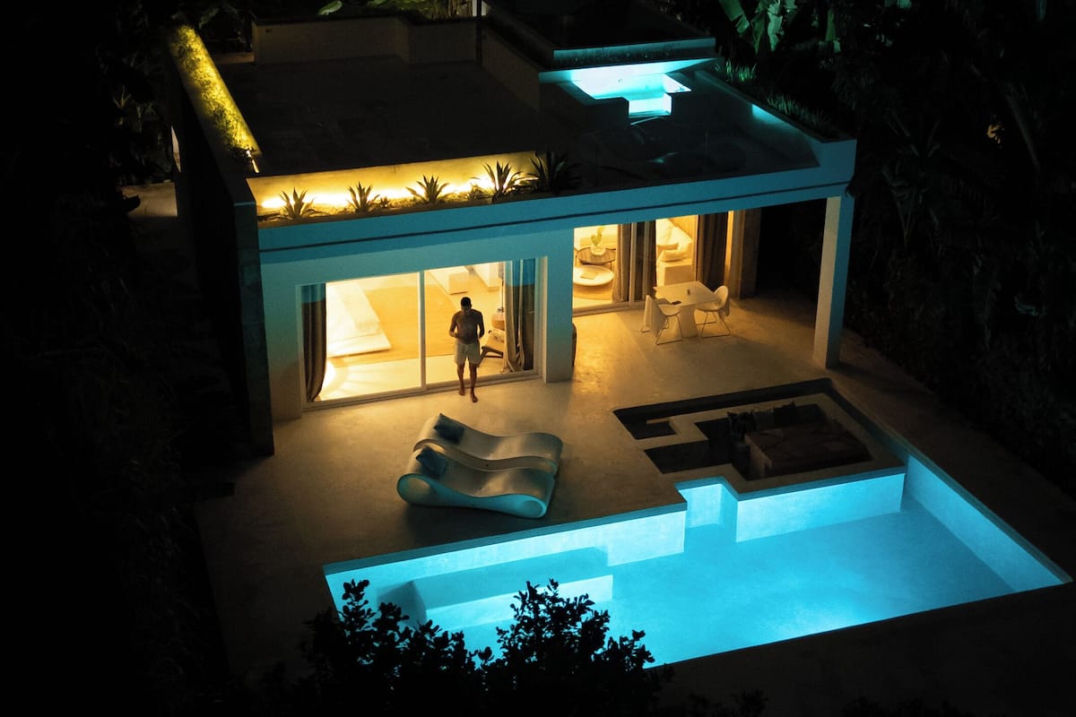 Ein modernes Haus mit Swimmingpool, eine Person draußen und ein gut beleuchtetes Interieur.