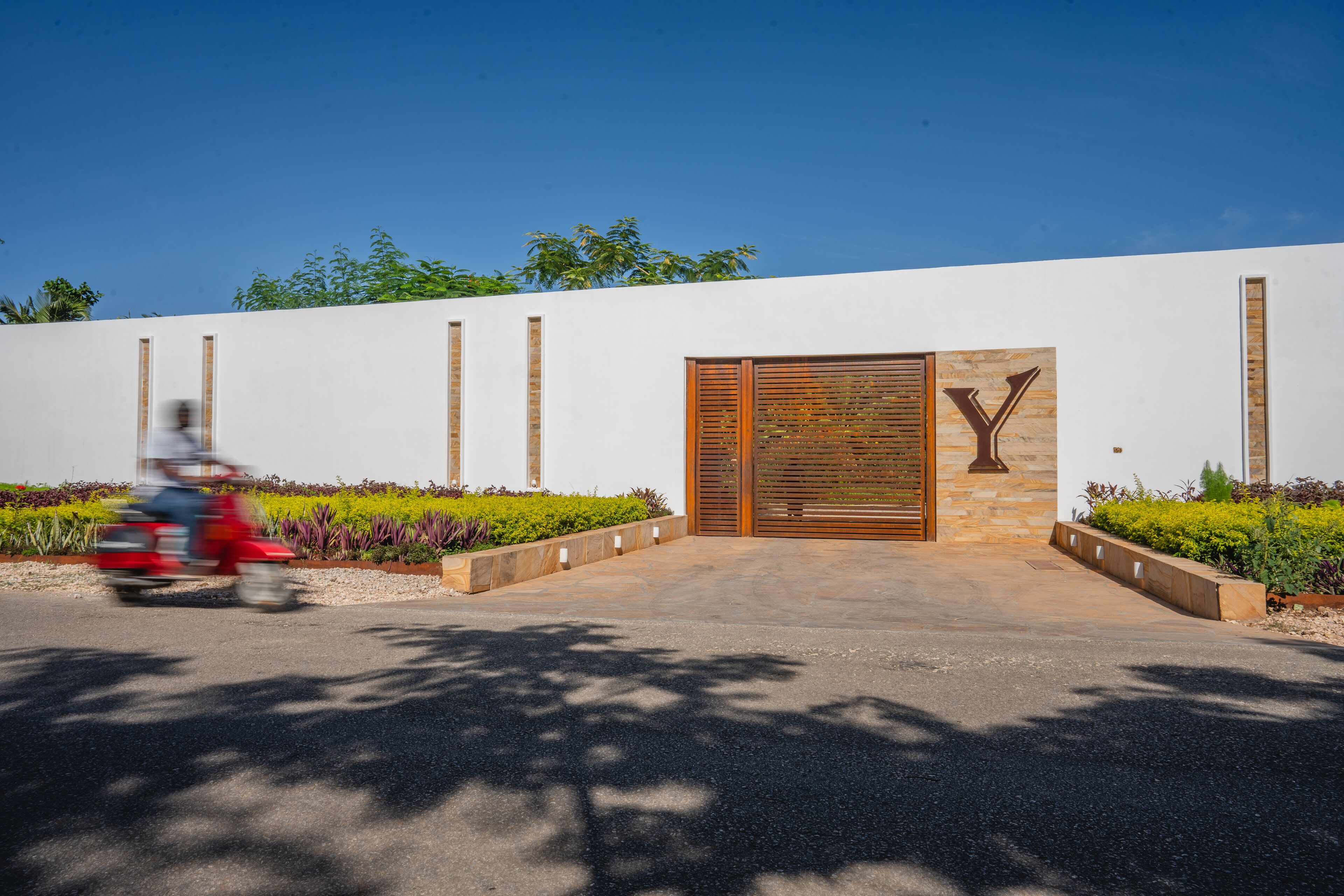 A modern building with a prominent 'Y' logo, a gated entrance, and a landscaped garden area.