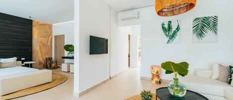 A modern living room with a sofa, a coffee table with fruit, a hanging light, and a TV on the wall.