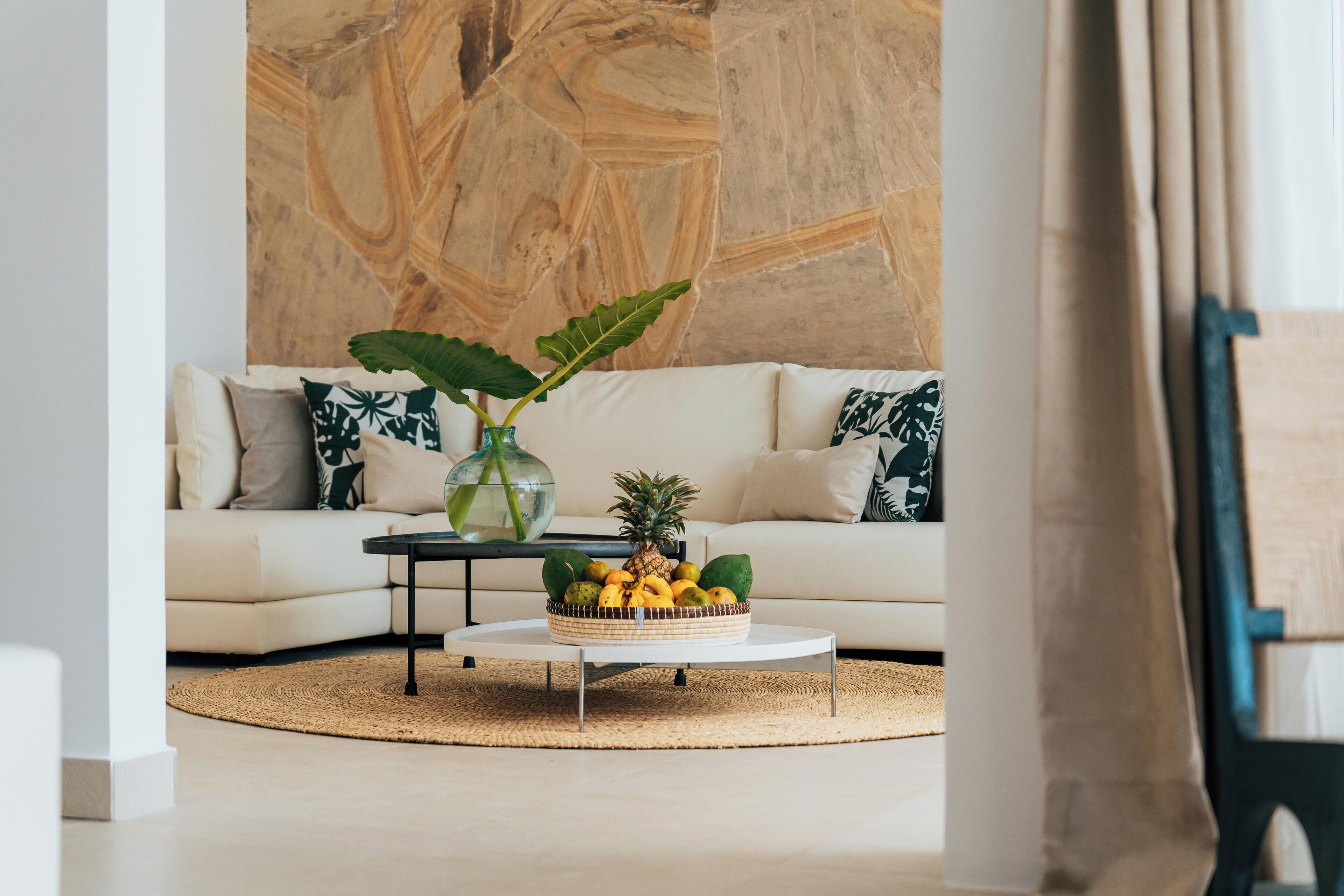 A living room with a white sofa, a coffee table with a fruit bowl, and a large abstract wall painting.