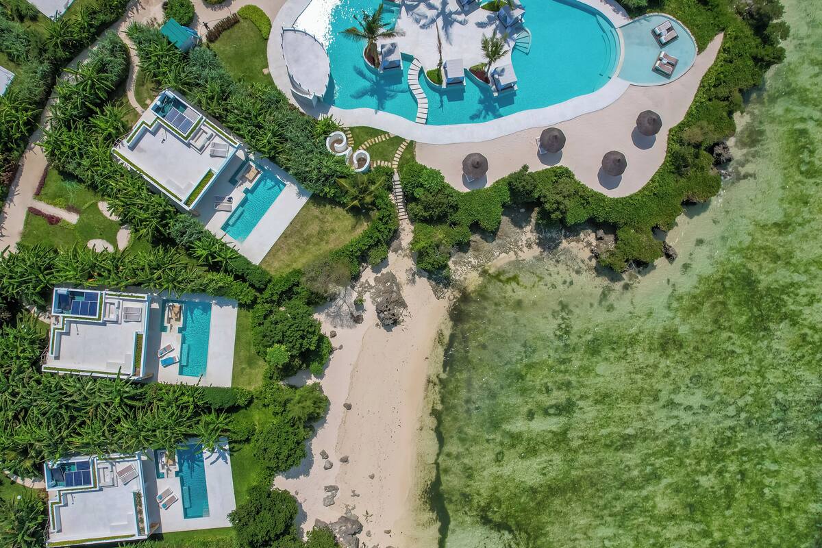 Eine Vogelperspektive zeigt einen luxuriösen Urlaubsort mit mehreren Schwimmbecken, Strandabschnitten und üppiger Vegetation.