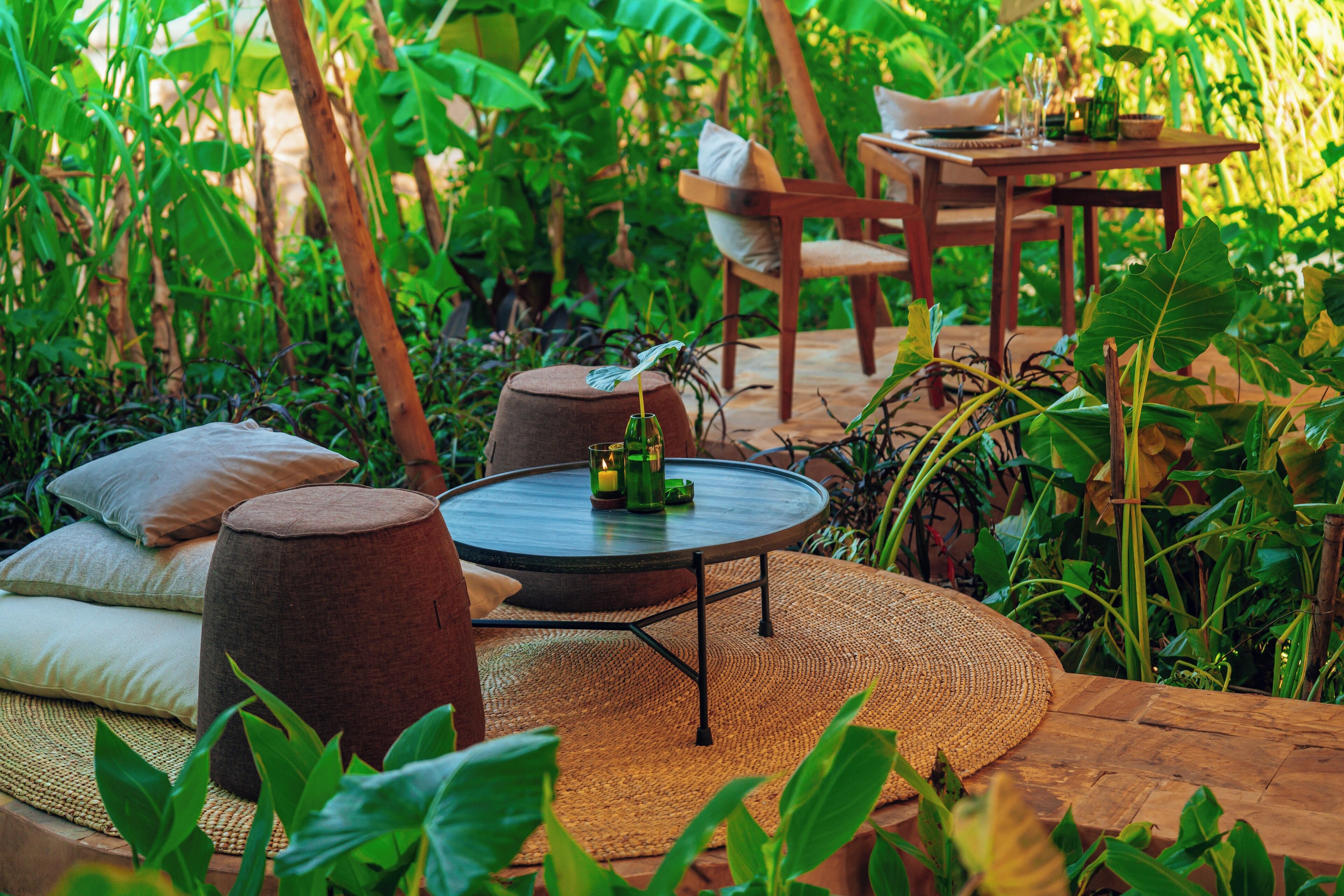 An outdoor seating area with a round table, cushioned stools, and a wooden table with chairs.