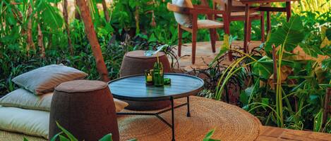 An outdoor seating area with a round table, cushioned stools, and a wooden table with chairs.