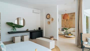 A modern hotel room with a bed, a vanity with a mirror, a round mirror, a small plant, a round table with a fruit bowl, and a sofa.