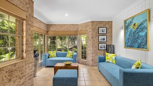 A room with brick walls, large windows, a blue sofa set, and a painting of fish. - Palm Beach House - Red Rock location (Red Rock)