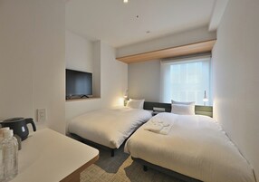 Quarto de hotel com duas camas, televisão, mesa com chaleira e janela com vista.