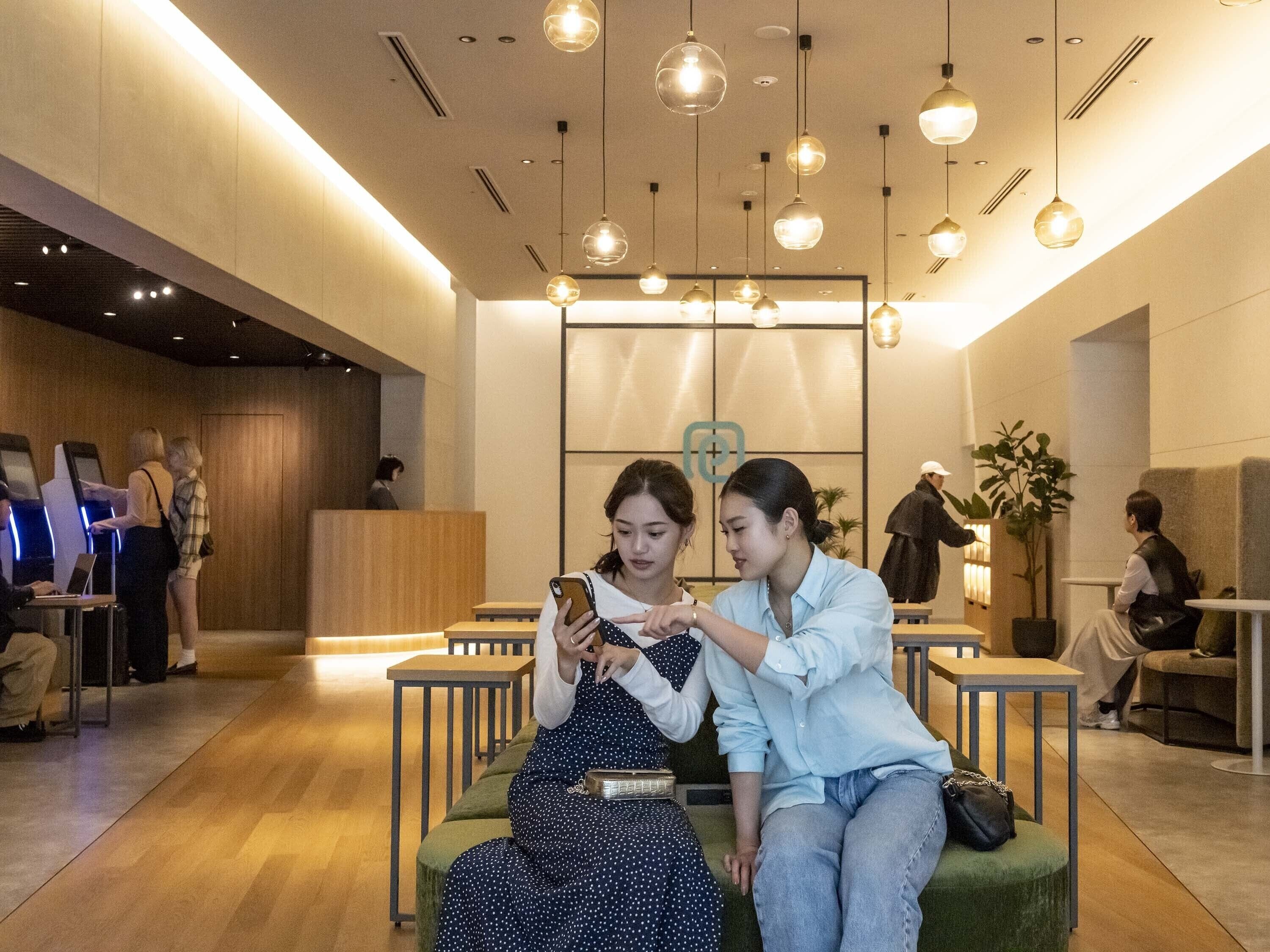 A modern hotel lobby with seating areas, a reception desk, and a digital check-in kiosk.