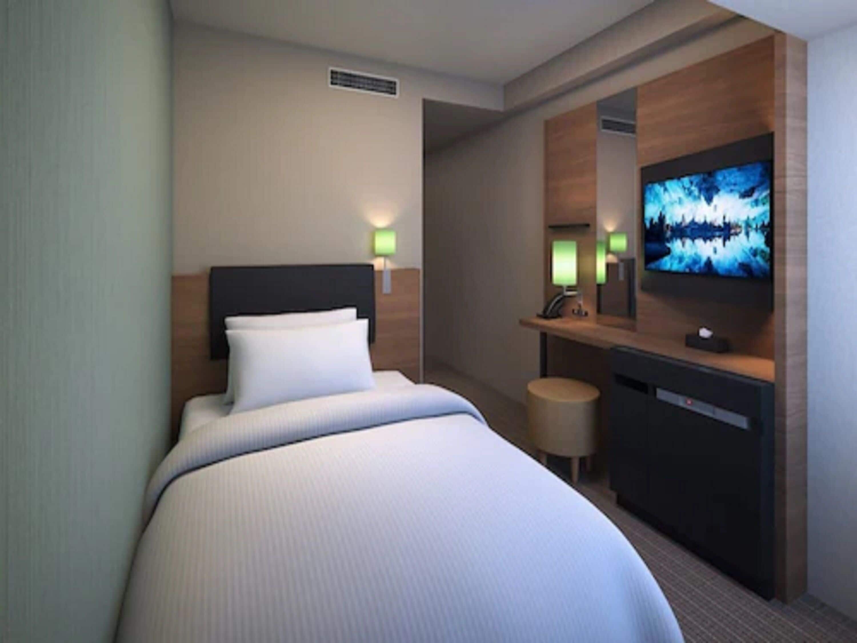 A hotel room with a bed, a TV, a desk with a mirror, and two wall-mounted lamps.