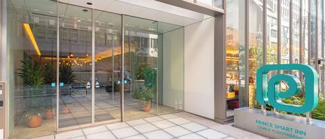 A modern hotel entrance with glass doors, potted plants, and a sign for the Prince Smart Inn in Osaka.