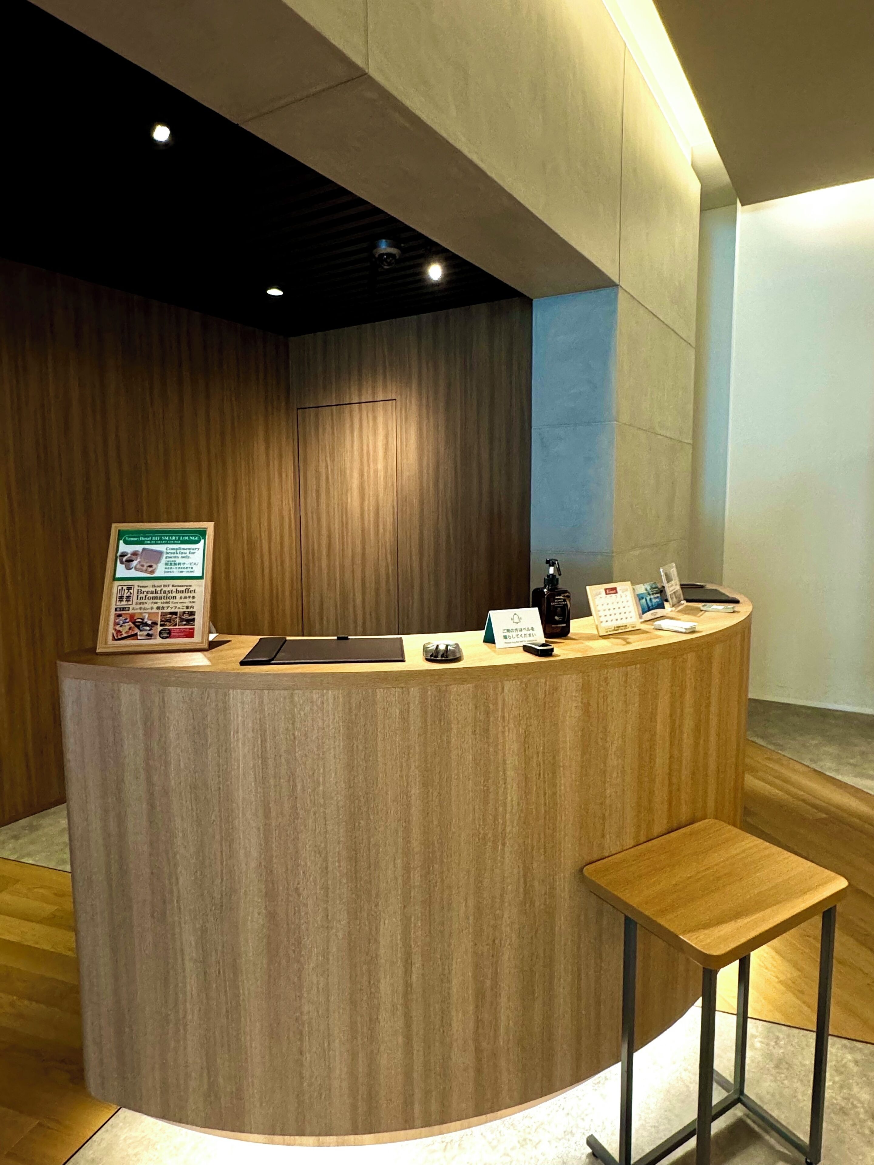 A reception desk with a wooden finish, a small stool, a calendar, and a sign with breakfast information.