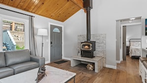 Un salon moderne avec une cheminée en pierre, un canapé gris et un plafond en bois.