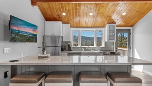 Une cuisine moderne dotée d’un grand îlot central, d’un plafond en bois et offrant une vue magnifique par les fenêtres.