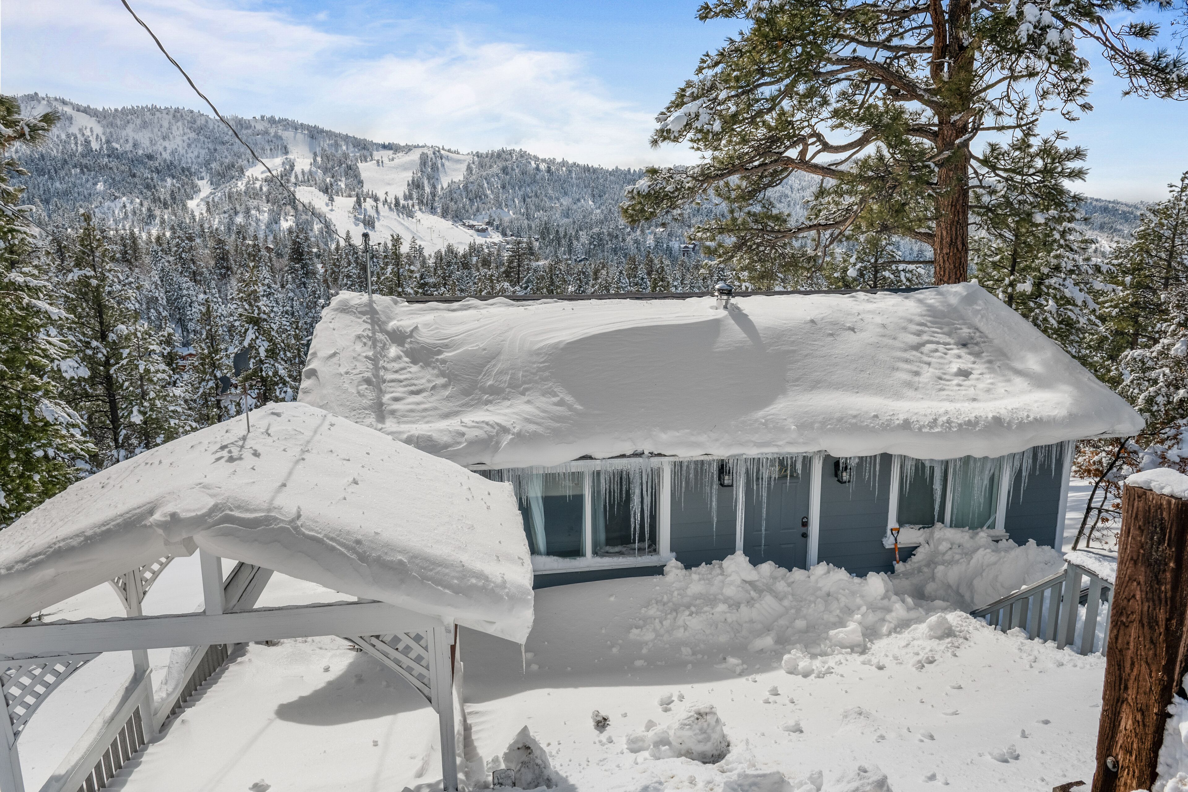 A snow-covered house with icicles hanging from the windows, surrounded by a snowy landscape and trees.