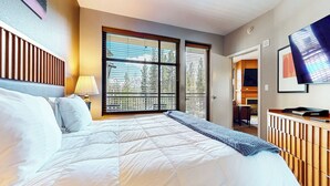 A hotel room with a bed, a window with blinds, a lamp, a TV, and a fireplace. - Pet-Friendly in Luxury Hotel. Across The Village, EV Charging Station On-site (Mammoth Lakes)