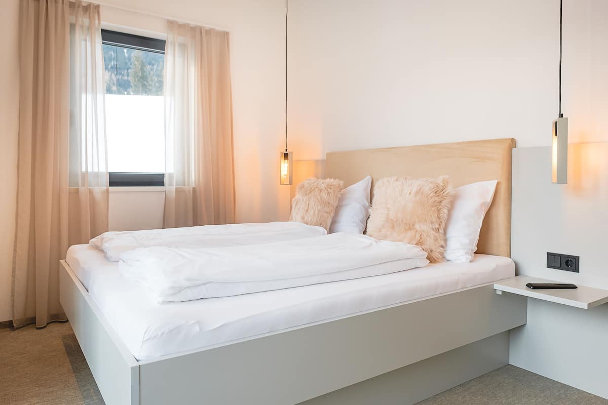 A modern bedroom with a large bed, a bedside table, and a window with curtains.
