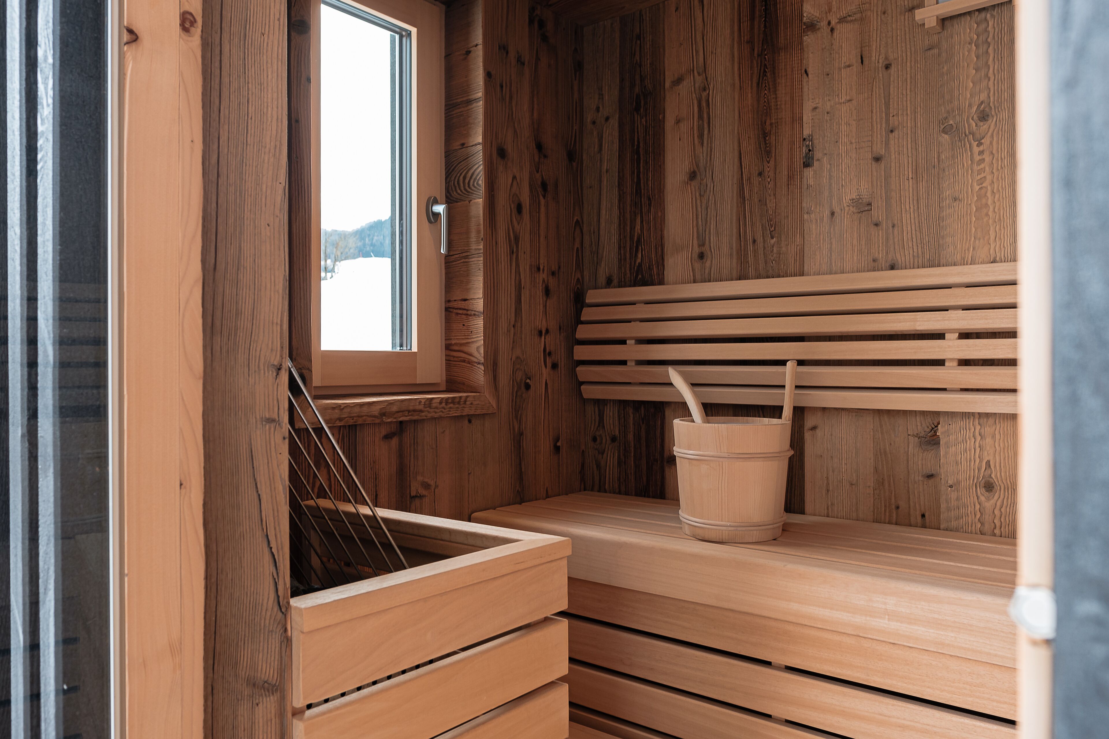 Un sauna avec des murs et des bancs en bois, une fenêtre et un seau.
