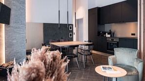 Une cuisine moderne avec des meubles de rangement sombres, une table à manger en bois et des chaises. On y trouve une petite table ronde sur laquelle est posé un magazine.