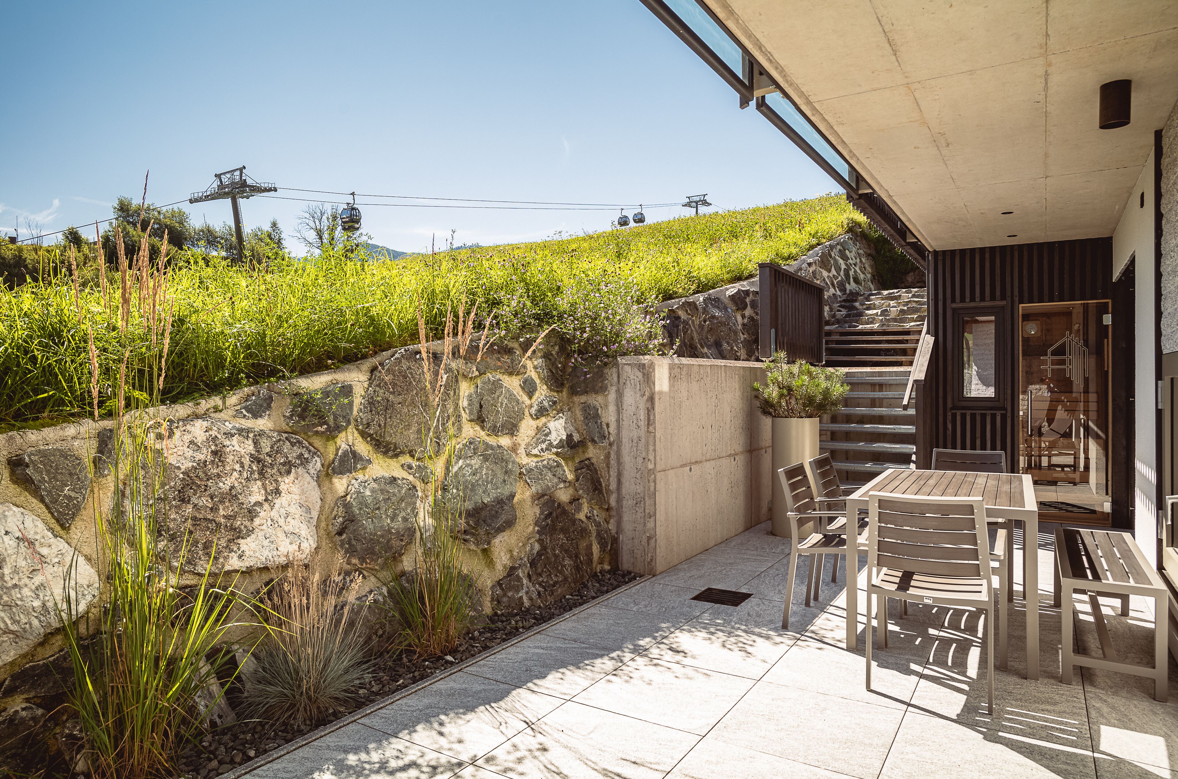 A patio area with outdoor seating, a stone wall, and a view of a cable car in the background.
