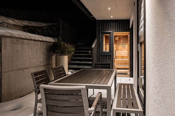 Un patio con mesa y sillas de madera, una planta en maceta y una escalera que lleva a un espacio interior.