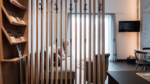 Un salon moderne doté d’une cloison en lattes de bois, d’un téléviseur à écran plat fixé au mur et d’un coin repas avec une table et des chaises.