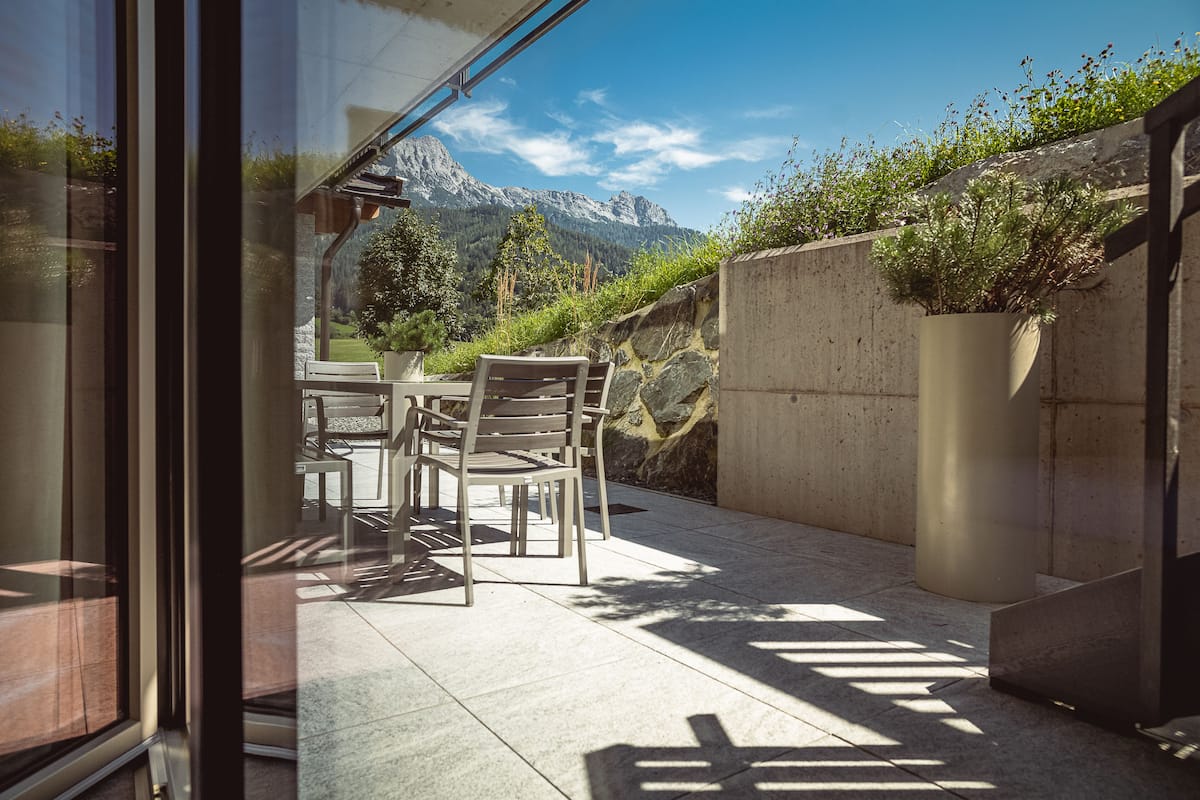 A patio with a table and chairs, a concrete wall, and a view of mountains.