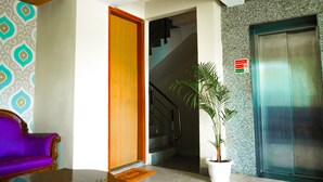 A hotel lobby with a purple sofa, a wooden door, a staircase, and an elevator. - JK Suites (Gurugram)