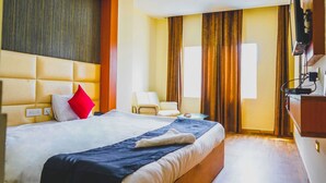 A hotel room with a large bed, a chair, a TV, and a window with curtains. - JK Suites (Gurugram)