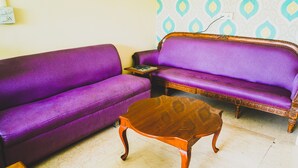 A room with two purple sofas, a wooden coffee table, and patterned wallpaper. - JK Suites (Gurugram)