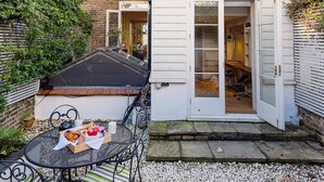 A courtyard with a table set for a meal, a door leading to a room, and a brick building with windows. - Notting Hill Townhouse - by Out of Office Lifestyle (London)