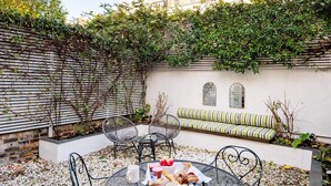 A patio with a round metal table, chairs, and a cushioned bench. - Notting Hill Townhouse - by Out of Office Lifestyle (London)