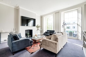 A modern living room with a sofa, armchairs, a coffee table, and a TV. - Notting Hill Townhouse - by Out of Office Lifestyle (London)