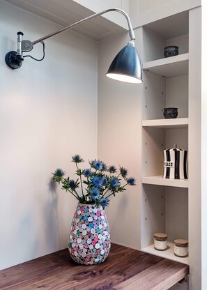 A wooden table with a colorful vase of blue flowers, a wall-mounted lamp, and shelves with decorative items. - Notting Hill Townhouse - by Out of Office Lifestyle (London)