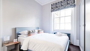A hotel room with a bed, bedside table, lamp, and a window with a view of buildings. - Notting Hill Townhouse - by Out of Office Lifestyle (London)
