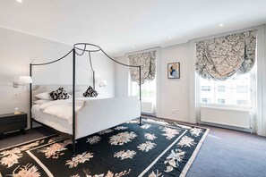 A four-poster bed with a dark floral carpet, a nightstand with a lamp, and a window with curtains. - Notting Hill Townhouse - by Out of Office Lifestyle (London)