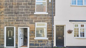 A two-story stone building with numbered doors, a window with blinds, and a door with a small plant. - Host & Stay | Waterlily Cottage (Stokesley)
