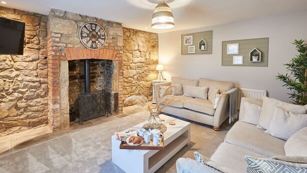 Un salon avec une cheminée en pierre, un canapé, une table basse sur laquelle se trouve un plateau avec divers objets, et des décorations murales.