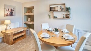 Un coin repas avec une table ronde en bois, dressée pour quatre personnes, des chaises blanches et un luminaire suspendu au-dessus.