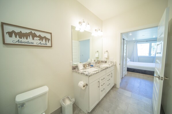 A bathroom with a toilet, sink, and mirror. There is a sign on the wall that reads "Adventure Awaits." - Modern Keystone Condo | Lake Fun + Hot Tubs (Keystone)