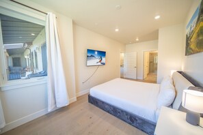 A bedroom with a large bed, a window with curtains, a painting on the wall, and a bathroom visible in the background. - Modern Keystone Condo | Lake Fun + Hot Tubs (Keystone)