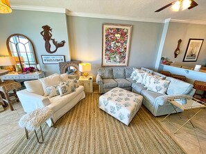 A living room with a sectional sofa, a small table, a lamp, and a decorative mirror. - Elegant, Stunning, Beach Front Condo; New to Rental Market! Oversized Balcony (Panama City Beach)