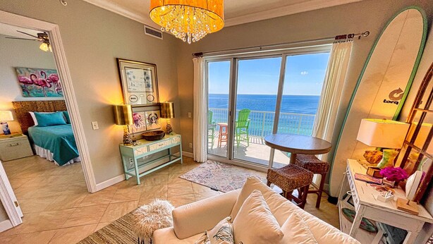 A spacious living room with a large window overlooking the ocean, a cozy seating area with a sofa and armchairs, and a dining area with a table and chairs. - Elegant, Stunning, Beach Front Condo; New to Rental Market! Oversized Balcony (Panama City Beach)