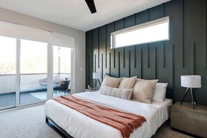 A modern bedroom with a large bed, a sliding glass door to a balcony, and a wall-mounted light fixture.