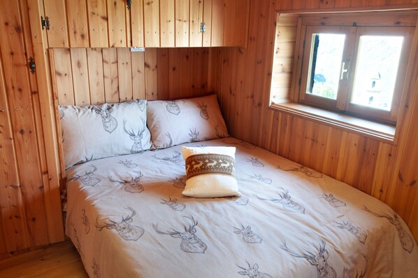 A wooden cabin bedroom with a bed, a window, and a wooden wardrobe.