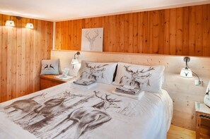 Een slaapkamer met houten lambrisering, een bed met beddengoed met hertenprint, bedlampen en een lijstwerk met kunst boven het bed.
