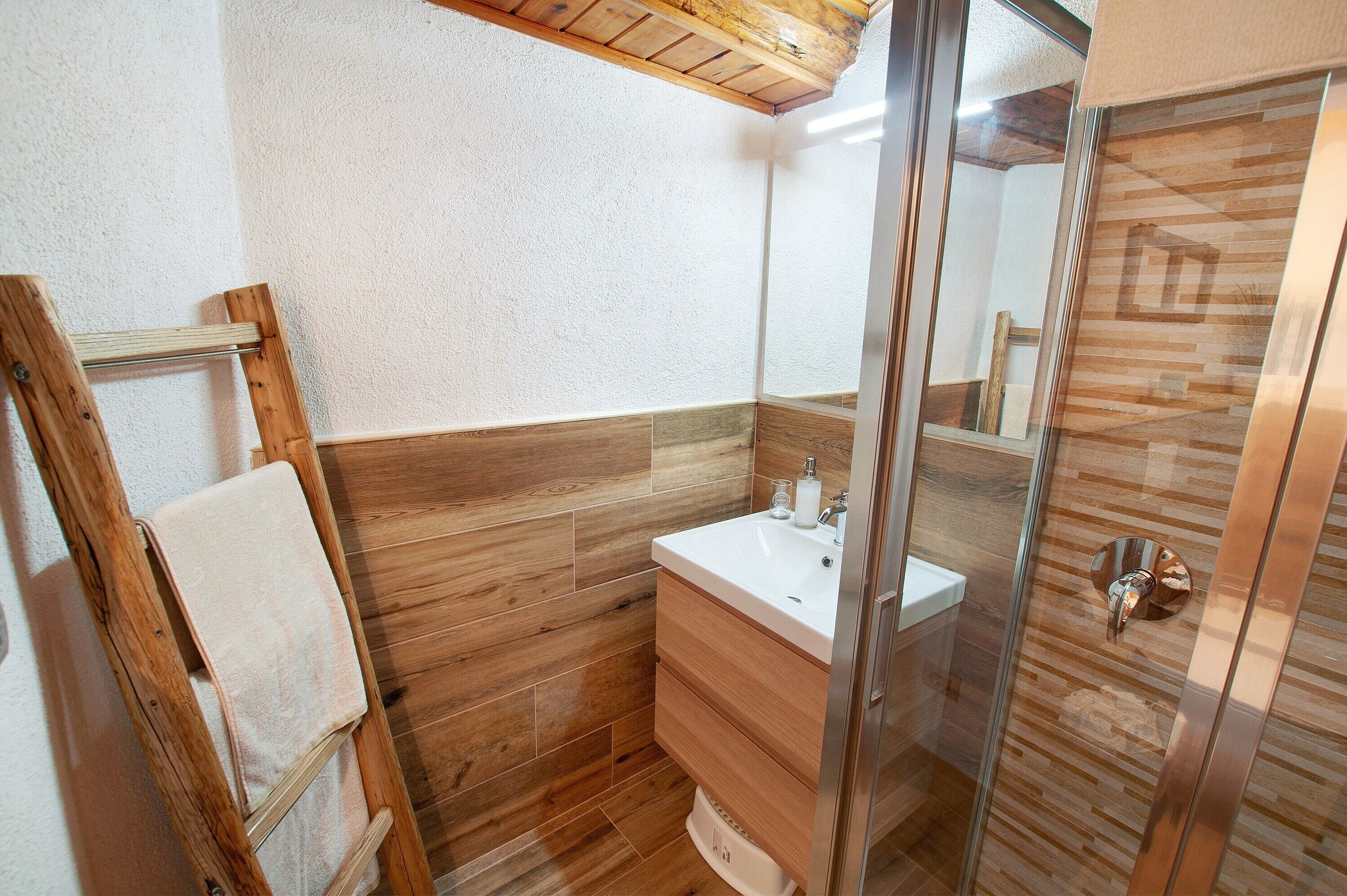 Ein Badezimmer mit Holzboden, einem weißen Waschbecken, einer Duschkabine aus Glas und einem Handtuchhalter.