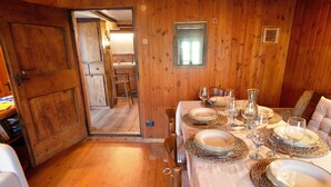 A wooden interior with a dining table set for four, a kitchen visible through an open door, and a small window. - Apartment "Sweet Somma Mountain Lodge 2" with Mountain View, Private Terrace & Wi-Fi (Sommarovina)