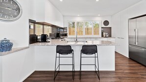 A modern kitchen with a central island, two bar stools, a large clock, and a stainless steel refrigerator. - Hamptons Resort: 3  BR, 2  BA House in Sorrento, Sleeps 6 (Sorrento)
