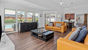 A spacious living room with a large window, a modern coffee table, a sofa, and a dining area. - Hamptons Resort: 3  BR, 2  BA House in Sorrento, Sleeps 6 (Sorrento)