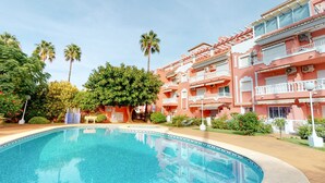 Un hôtel doté d’une piscine, de palmiers et d’un bâtiment rose agrémenté de balcons.